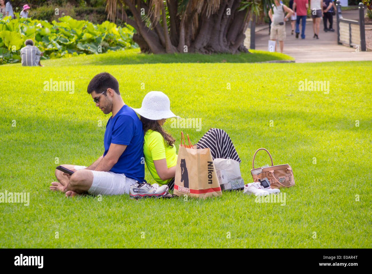 Sydney Australia,Royal Botanic Gardens,man men male,woman female women,couple,back to back,lawn,sitting,using,tablet,park,AU140309172 Stock Photo