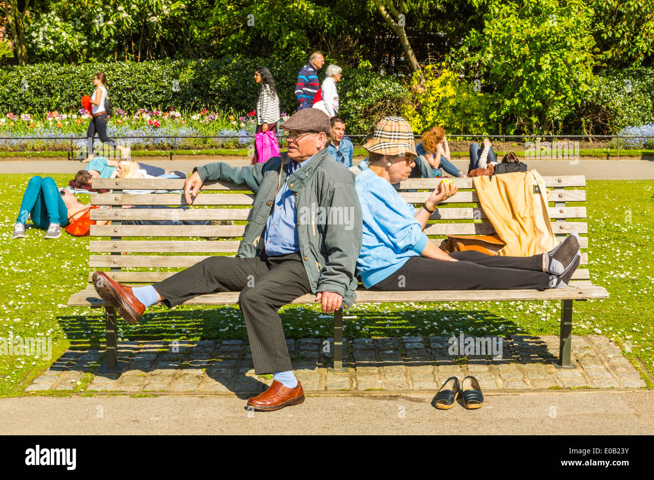 A senior Couple sitting and relaxing in the sunshine on a park bench, Regents Park London,England UK Stock Photo