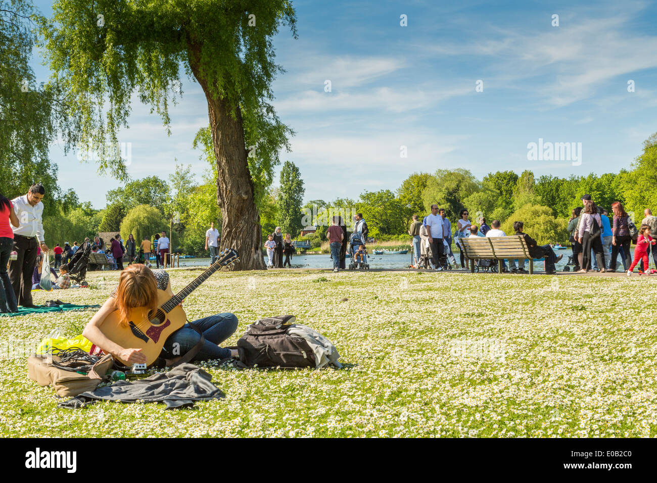 A Young Woman sitting and playing the guitar beside the lake in The Regents Park London England UK Stock Photo