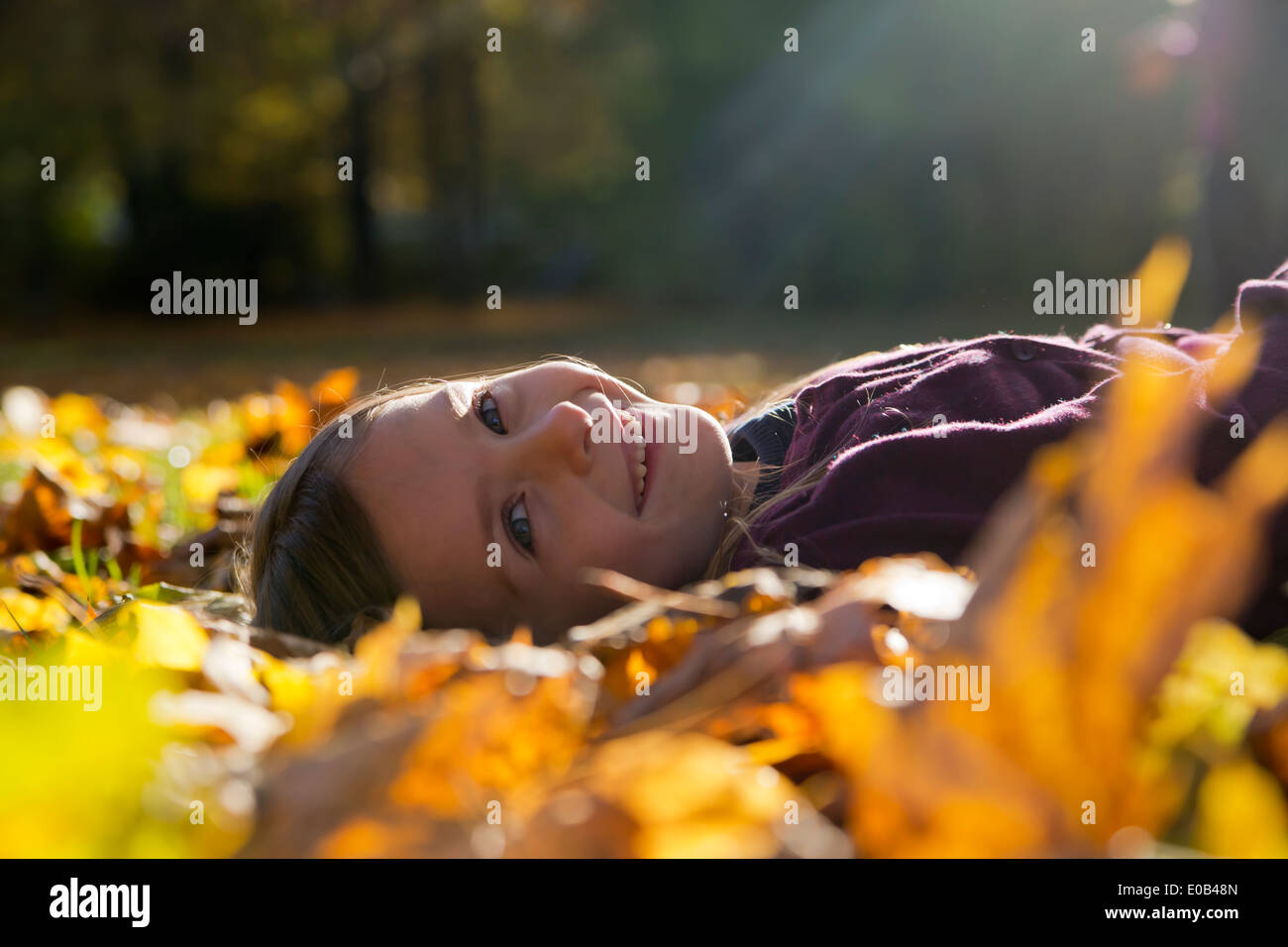 Portrait of smiling little girl lying on autumn leaves in park Stock ...