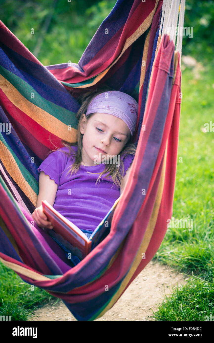 Portrait of little girl reading book in hammock Stock Photo - Alamy