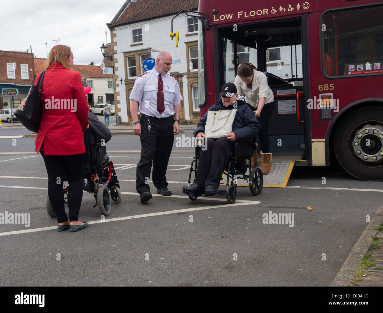 Two disabled people in wheelchairs with their carers being helped to board a bus by its driver Stock Photo