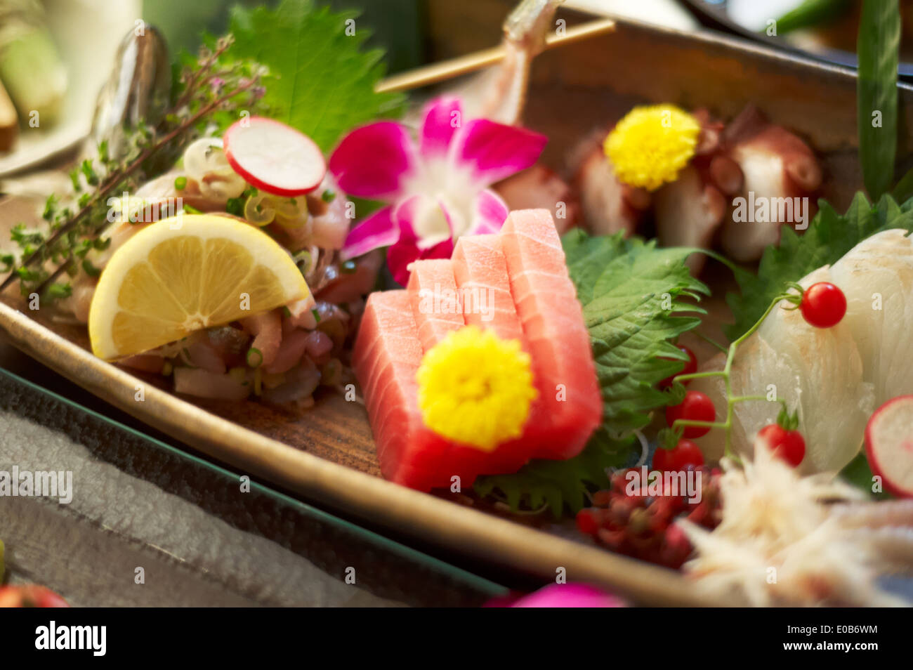 Still life of rustic food with sliced raw fish, fruit and flowers Stock Photo