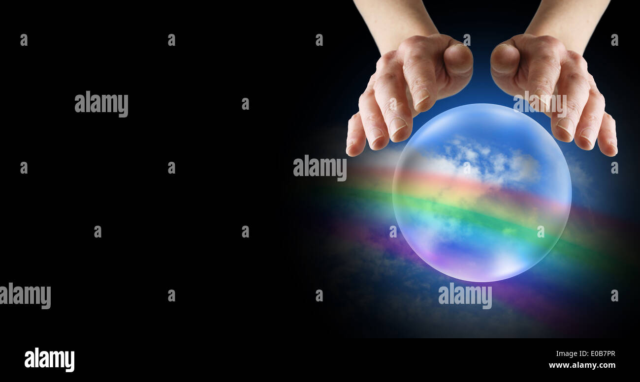 Female Clairvoyant's hands hovering over crystal ball showing rainbow and blue sky Stock Photo