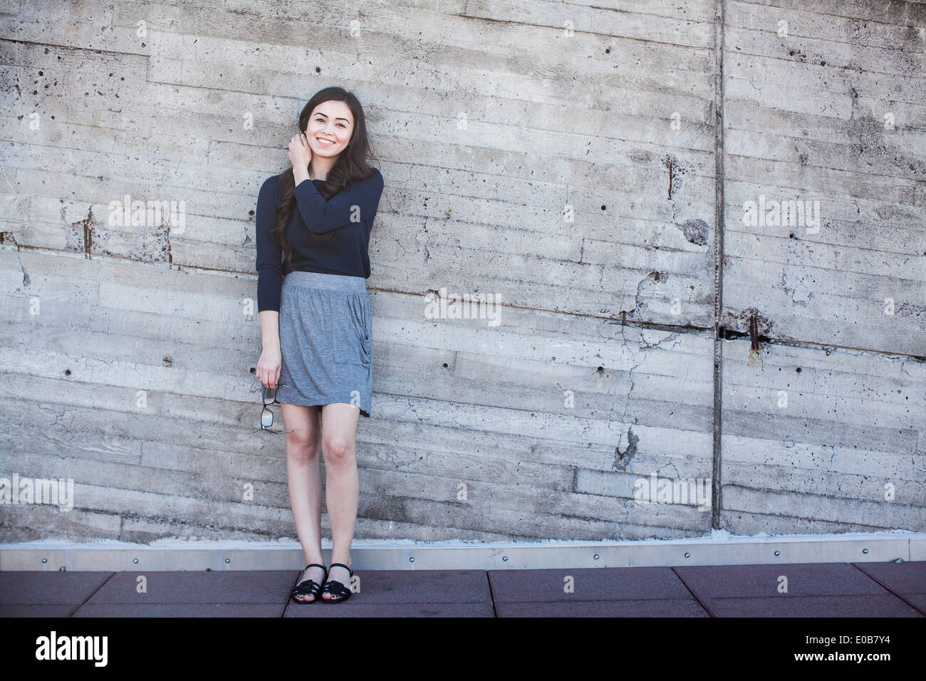 Young woman standing, leaning against wall Stock Photo