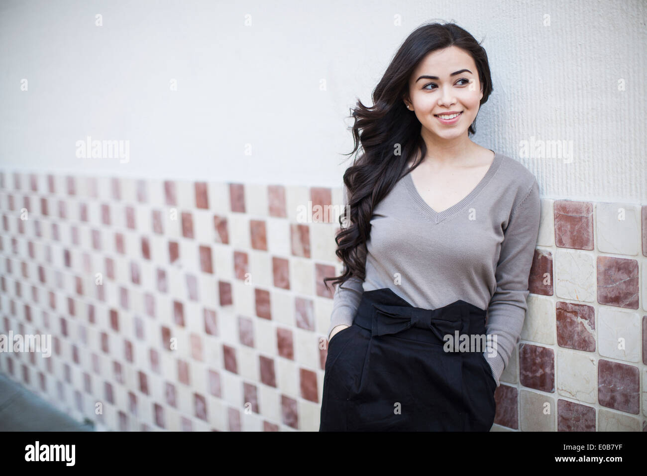 Portrait of young woman, leaning against tiled wall Stock Photo