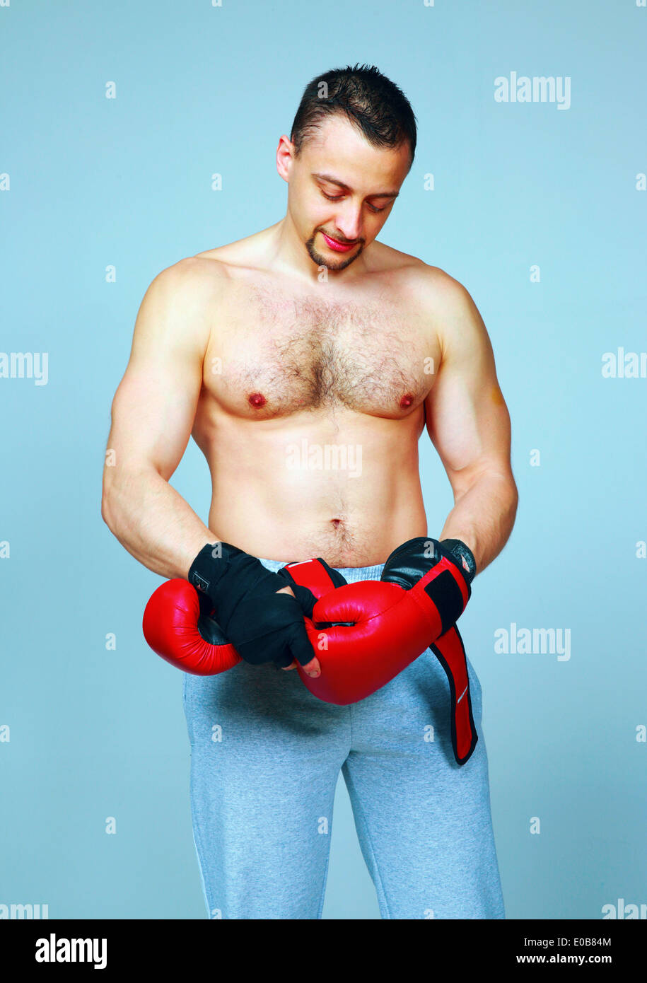 Fit man putting his boxing gloves, preparing for training over blue background Stock Photo