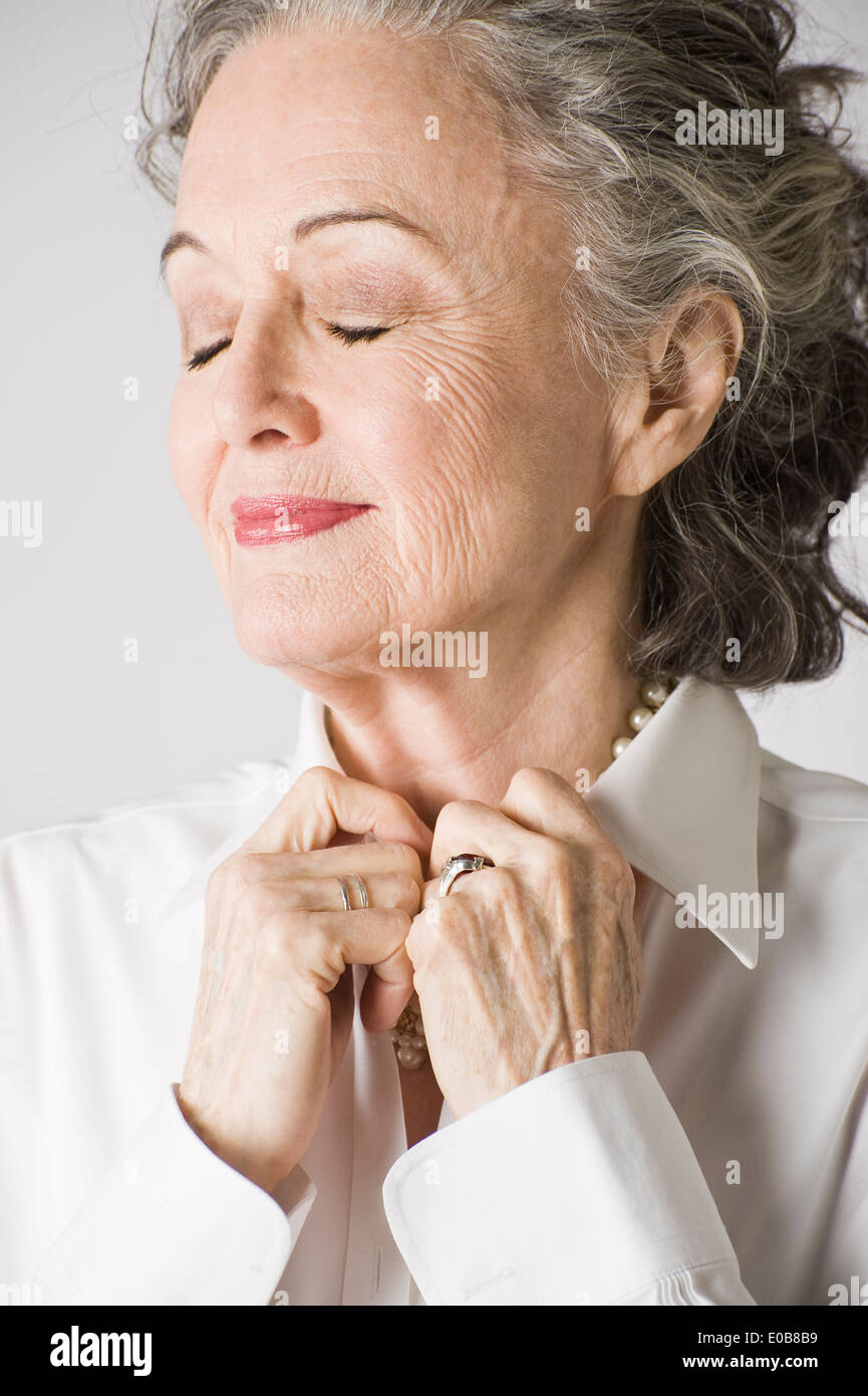 Portrait of senior woman, hands on collar, eyes closed Stock Photo