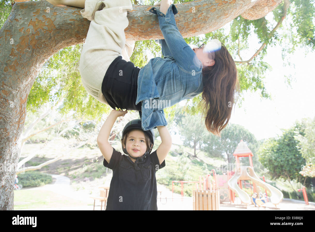 Upside down mother wrapped around tree branch with son helping Stock Photo
