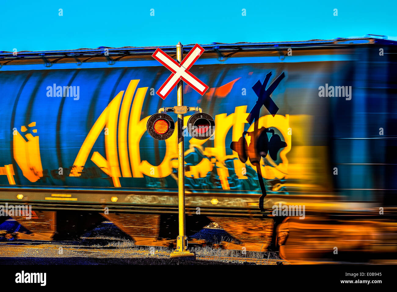 Colorful rail car moving past a crossing, with stop signal lights flashing Stock Photo