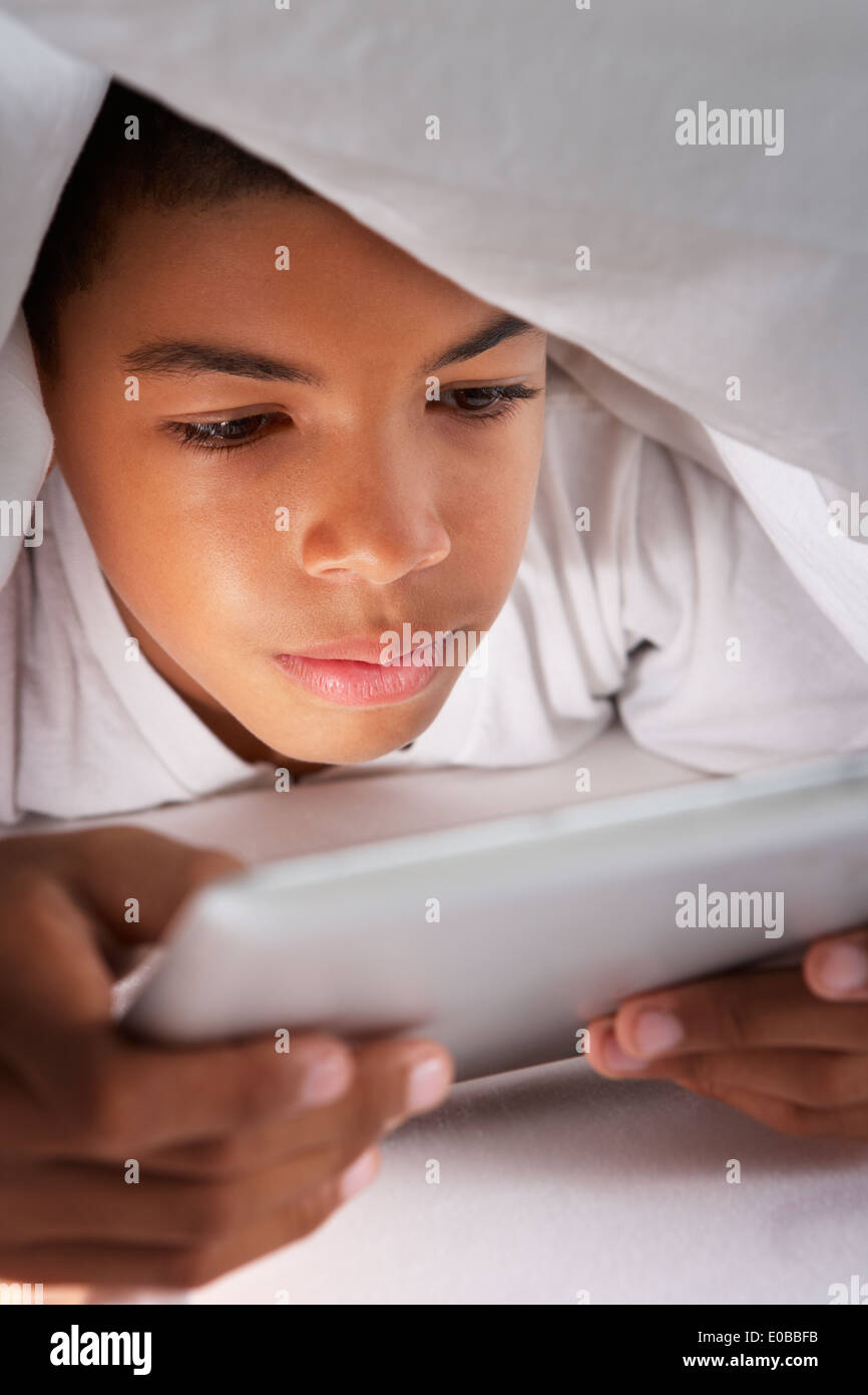 Boy Using Digital Tablet Under Duvet Stock Photo