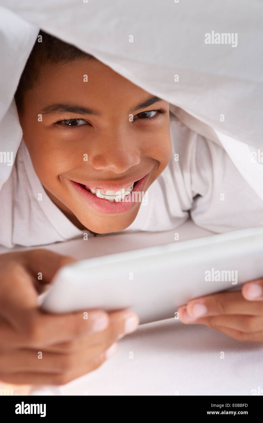 Boy Using Digital Tablet Under Duvet Stock Photo