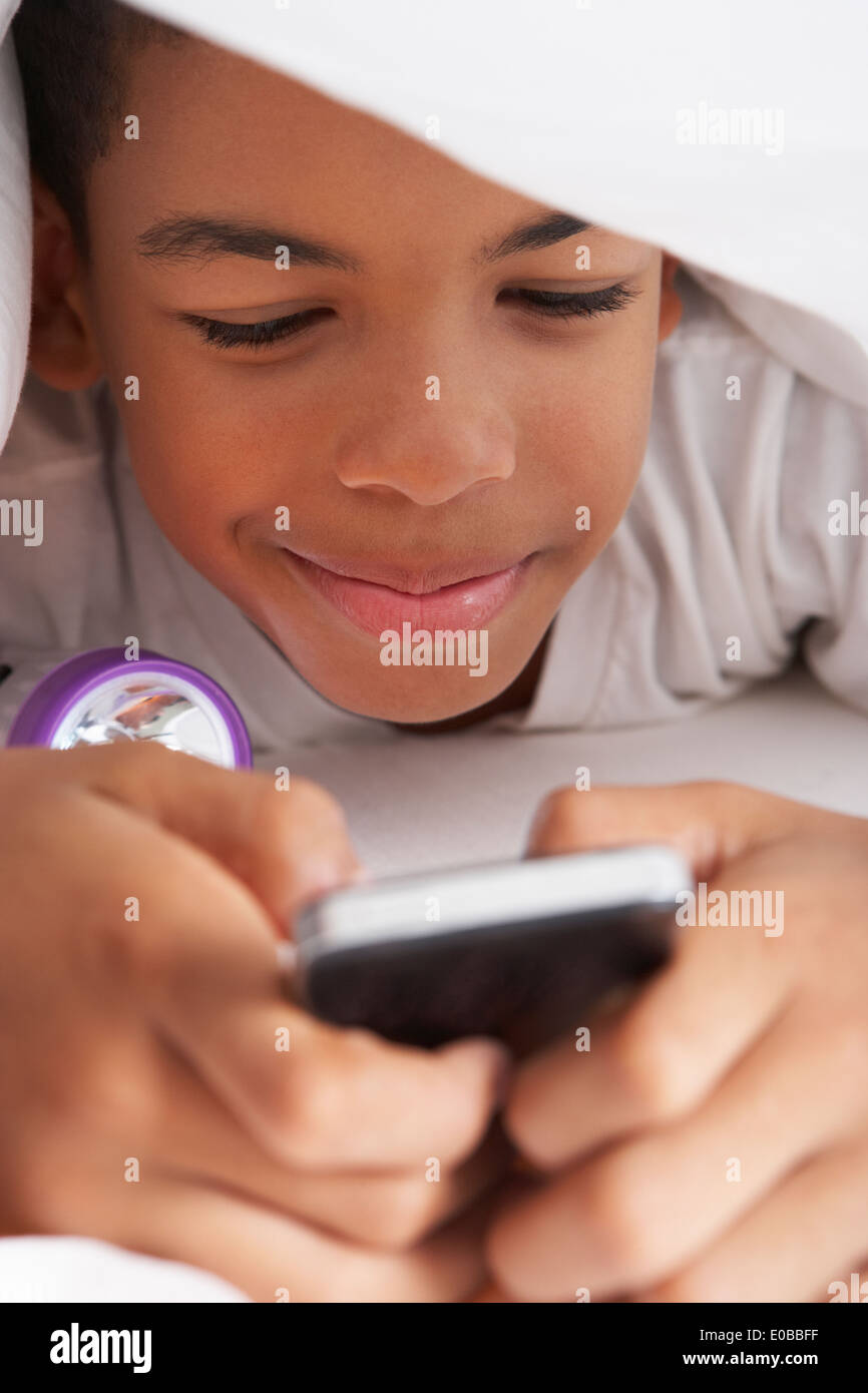 Boy Using Mobile Phone Under Duvet Stock Photo