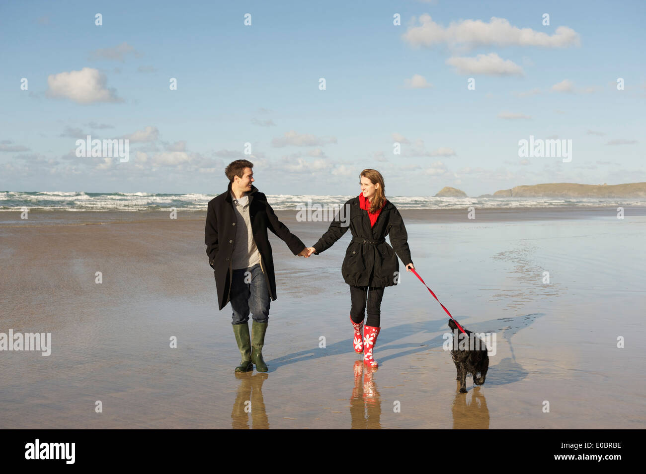 Young Romantic Couple walking their dog on a Beautiful Cornish Beach Stock Photo