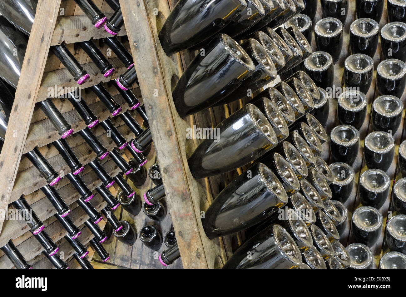 Dusty bottles with brut sparkling wine on wooden rack in winery vault Stock Photo