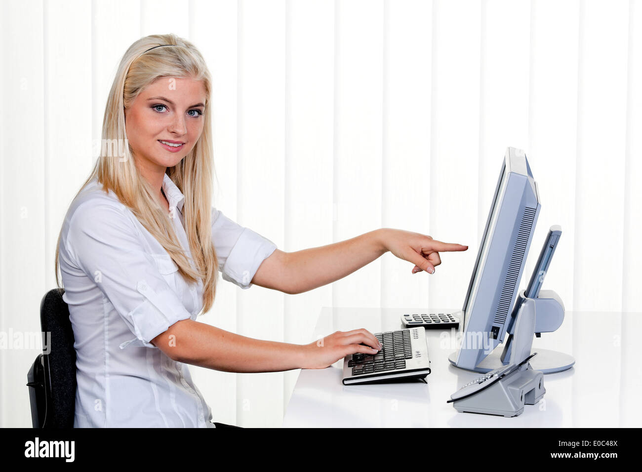Young woman with computer in the office. Before bright background, Junge Frau mit Computer im Buero. Vor hellem Hintergrund Stock Photo