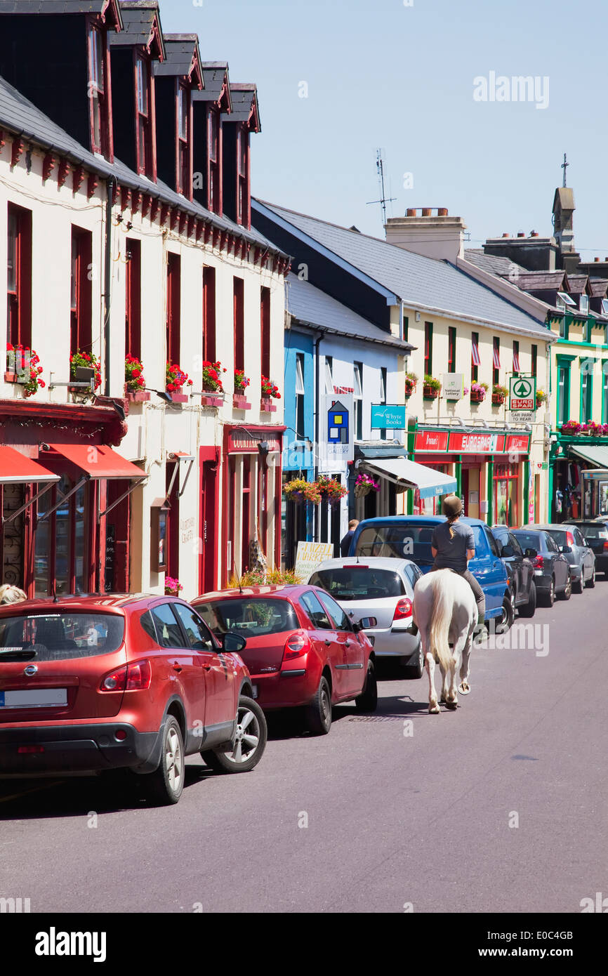 Riding a horse up the street beside parked cars and retail shops