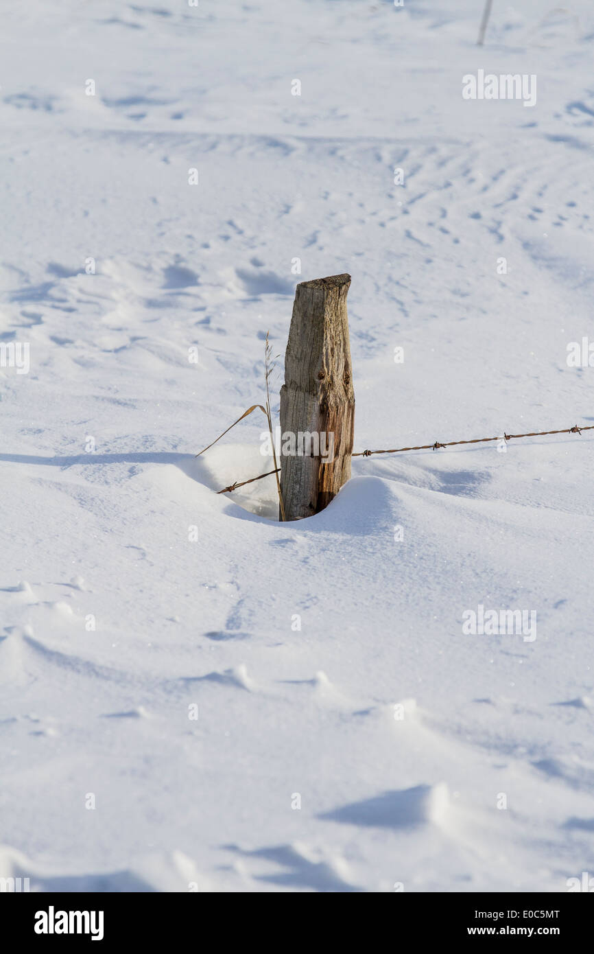 Fence post, in rural Alberta, almost buried by snow, showing drifting results. Stock Photo