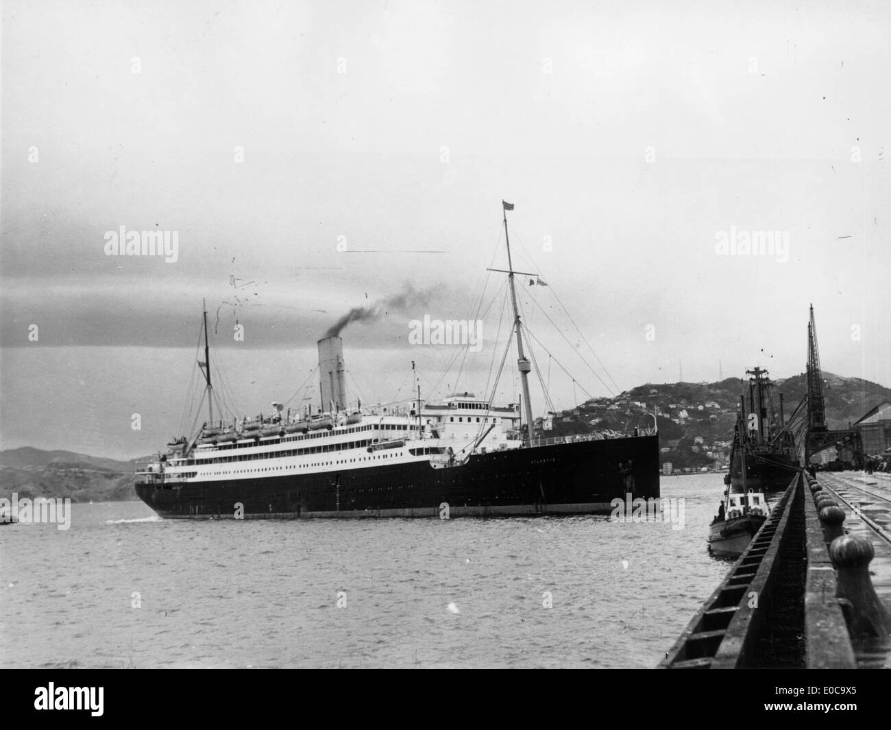The RMS Atlantis, an armed merchant cruiser, is pictured docked in Wellington Harbour, New Zealand, in 1951. This vessel was part of the Royal Mail Lines, serving both commercial and military roles during the mid-20th century. Stock Photo