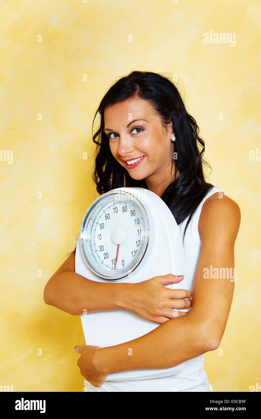 A young woman with scales in the hand smiles after successful diet, Eine junge Frau mit einer Waage in der Hand laechelt nach er Stock Photo