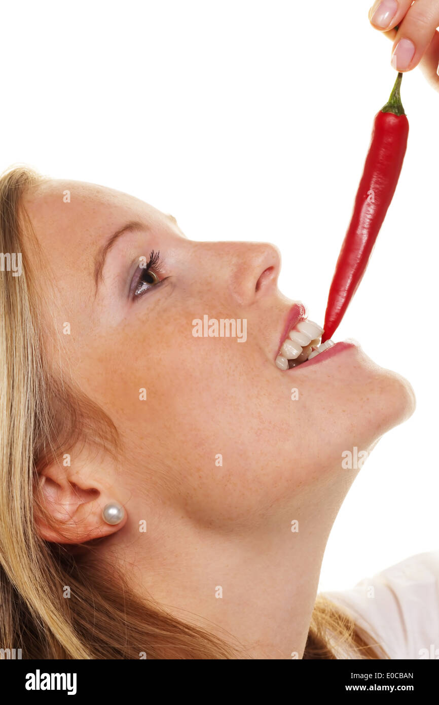 A young woman bites in a Chilli pod. Before white background, Eine junge Frau beisst in eine Chilli Schote. Vor weissem Hintergr Stock Photo