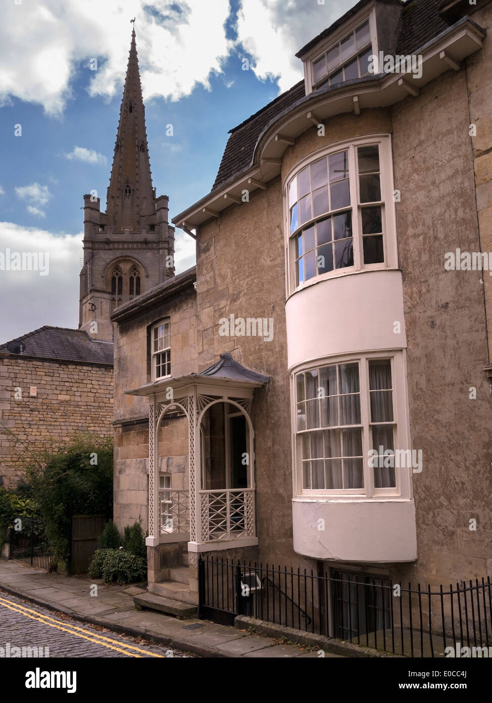 Old stone building with ornate porch and curved sash bay window and church tower beyond, Stamford, Lincolnshire, England, UK Stock Photo