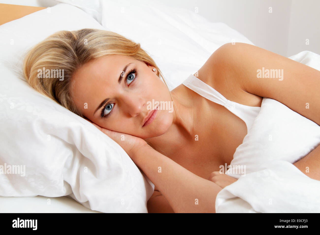 A young woman lies awake in the bed. Sleepless and thoughtfully. Stock Photo