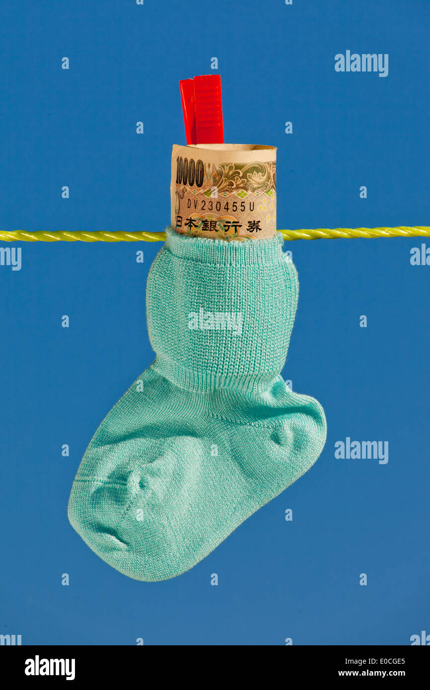 Baby socks on clothesline with yen to bank notes from Japan., Baby Socken auf Waescheleine mit Yen Geldscheinen aus Japan. Stock Photo