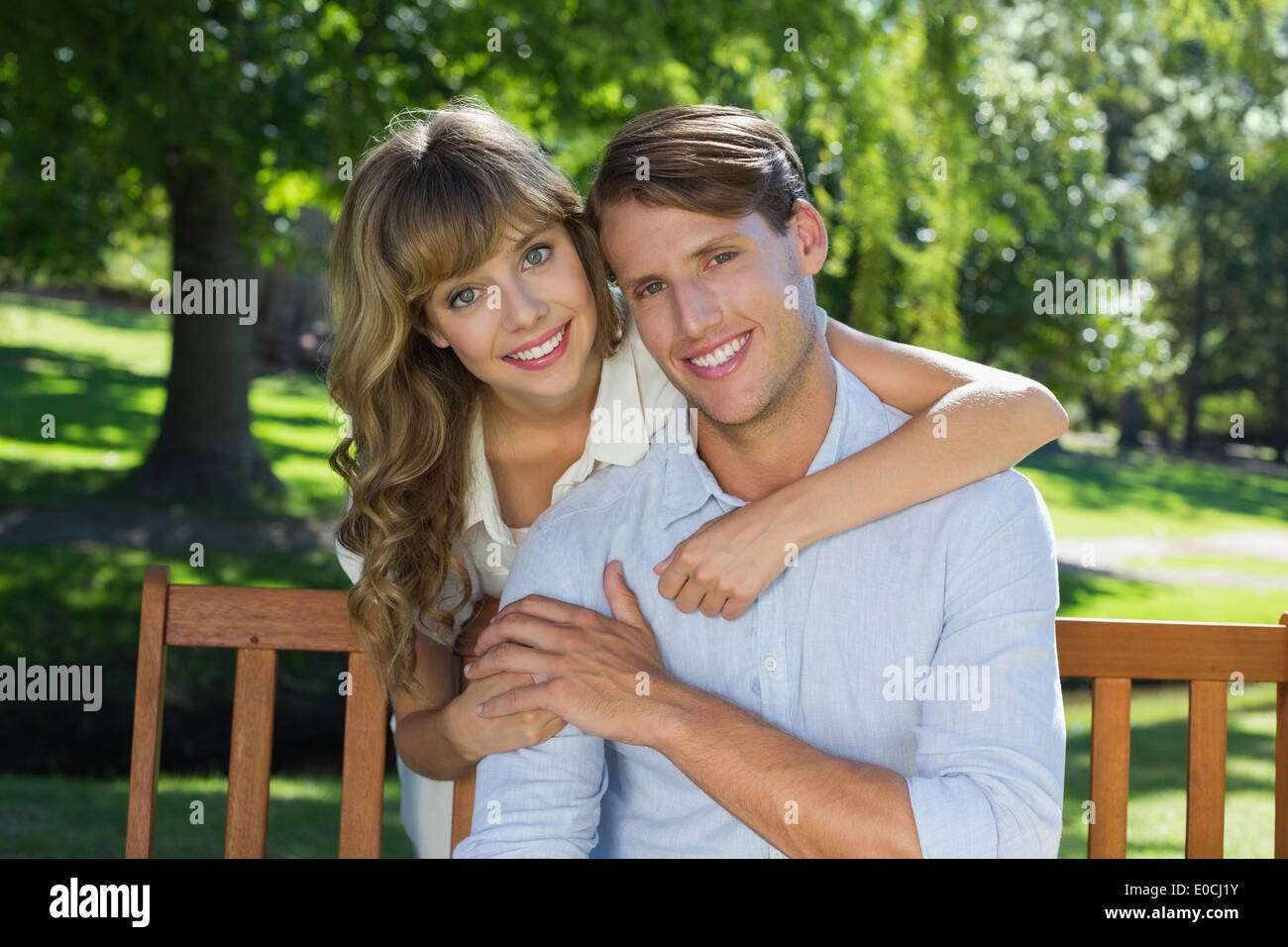 Affectionate couple relaxing on park bench together smiling at camera Stock Photo