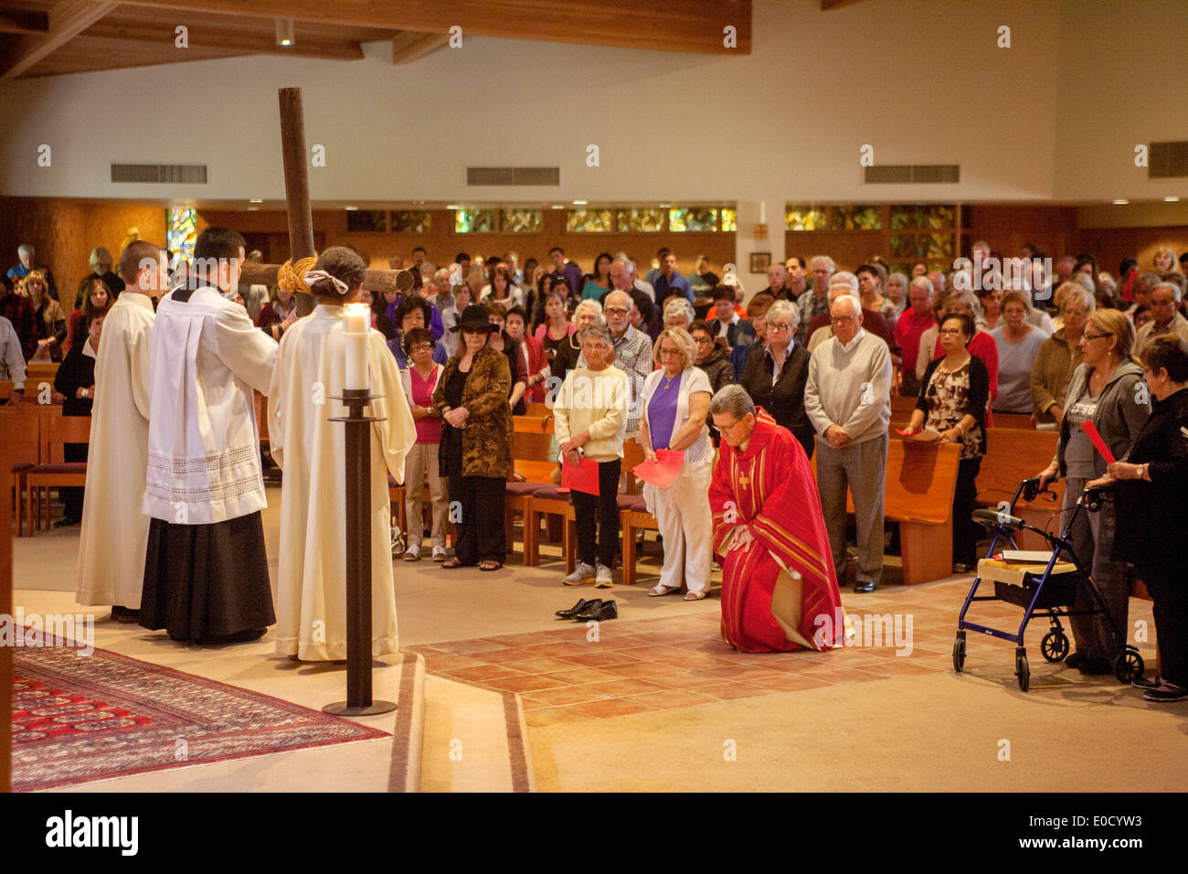 As the congregation watches, the pastor of St. Timothy's Catholic Church, Laguna Niguel, CA, kneels barefooted in the Solemn Veneration of the Cross during the Good Friday mass. Stock Photo
