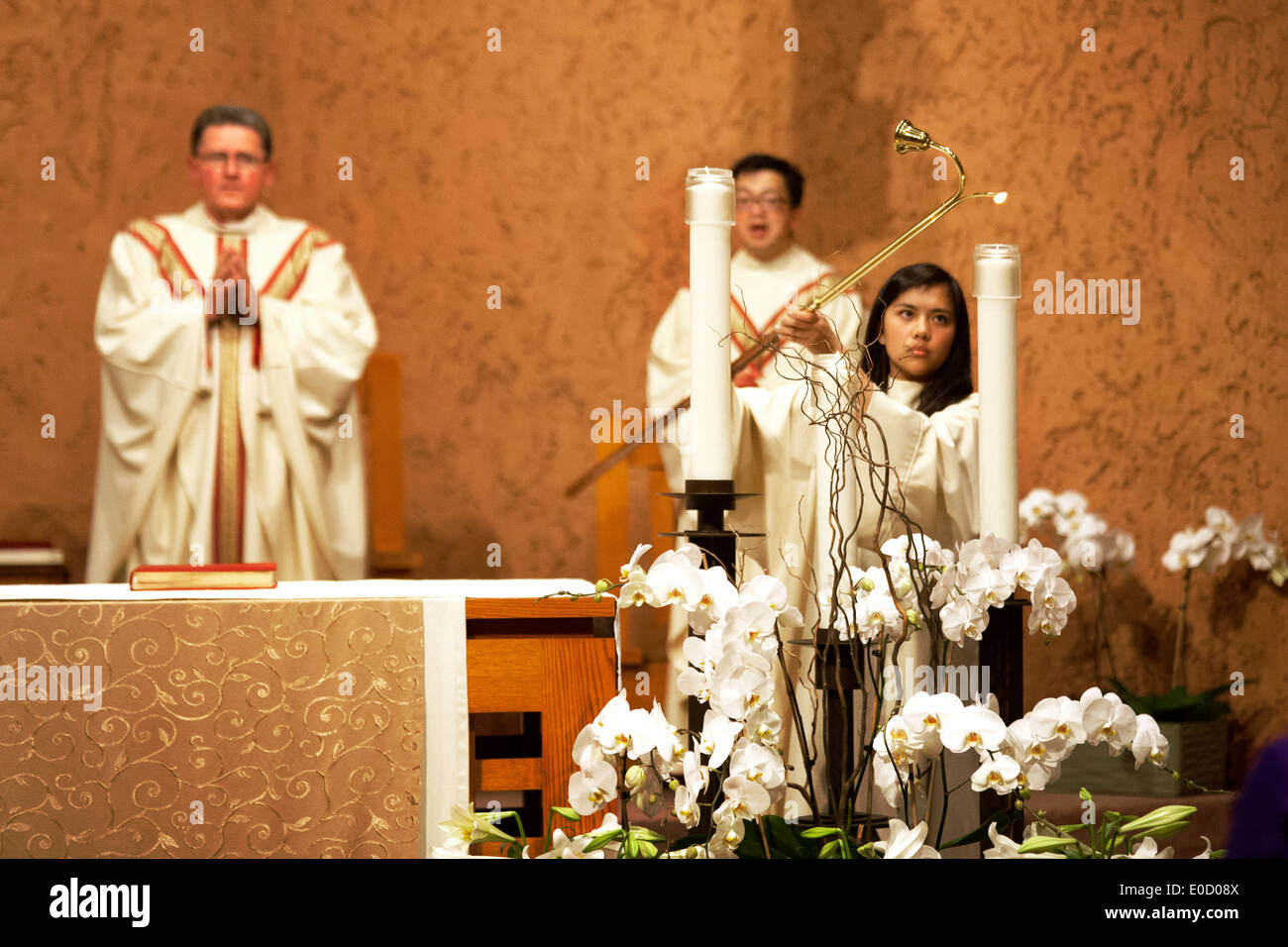 A young Hispanic altar server lights ceremonial candles at St. Timothy's Catholic Church, Laguna Niguel, CA, at the start of the Solemn Liturgy of Good Friday. Note pastor and Vietnamese assistant pastor in vestments. Stock Photo