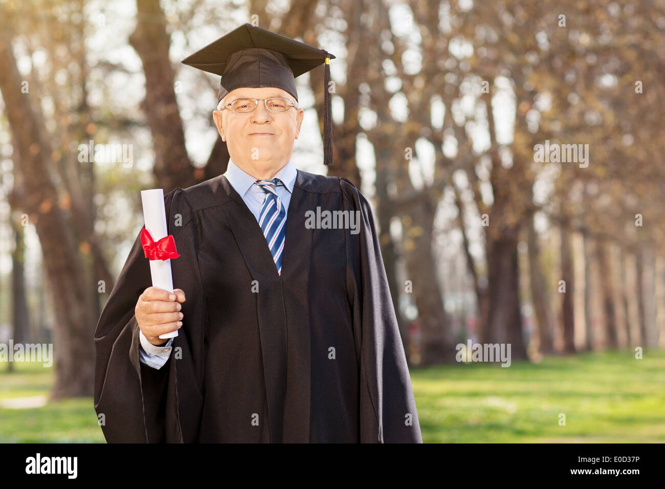Mature college graduate holding a diploma in park Stock Photo