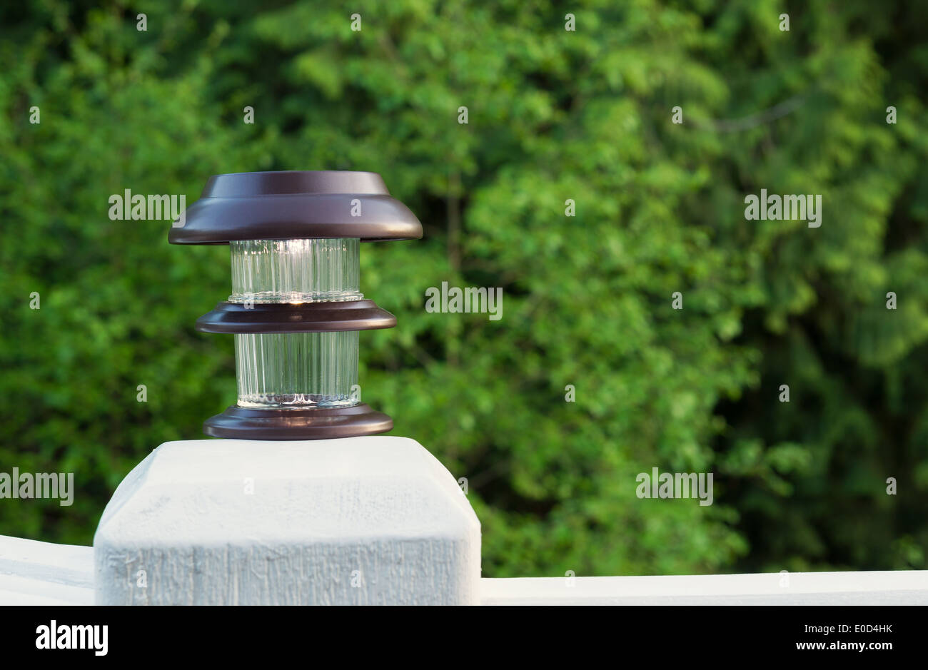 Horizontal photo of solar lamp, light just turning on, on patio post with green trees in background Stock Photo