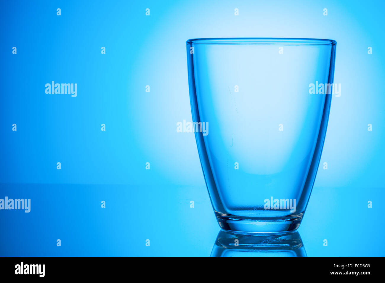 An empty glass stands before a blue background., Ein leeres Glas steht vor einem blauen Hintergrund. Stock Photo