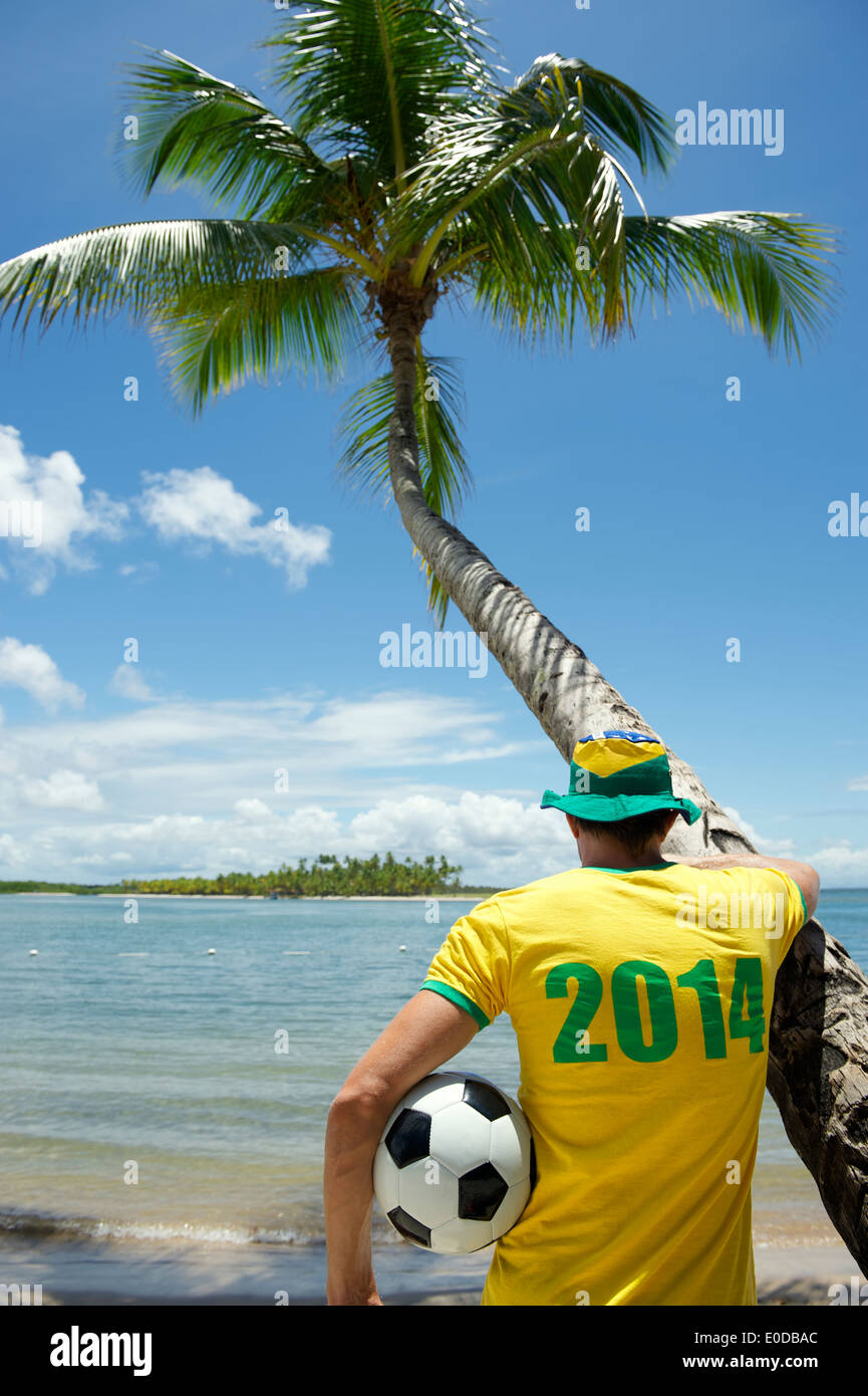 Brazilian football player in 2014 shirt holding soccer ball at palm tree on remote beach in Nordeste Bahia Brazil Stock Photo