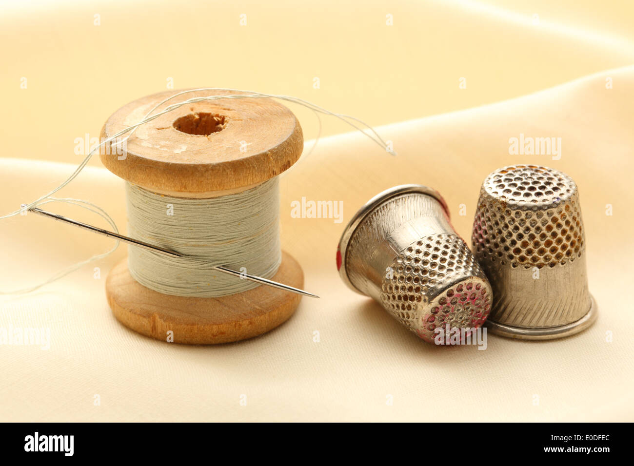 Sewing thimbles, bobbin and needle on silk cloth Stock Photo Alamy