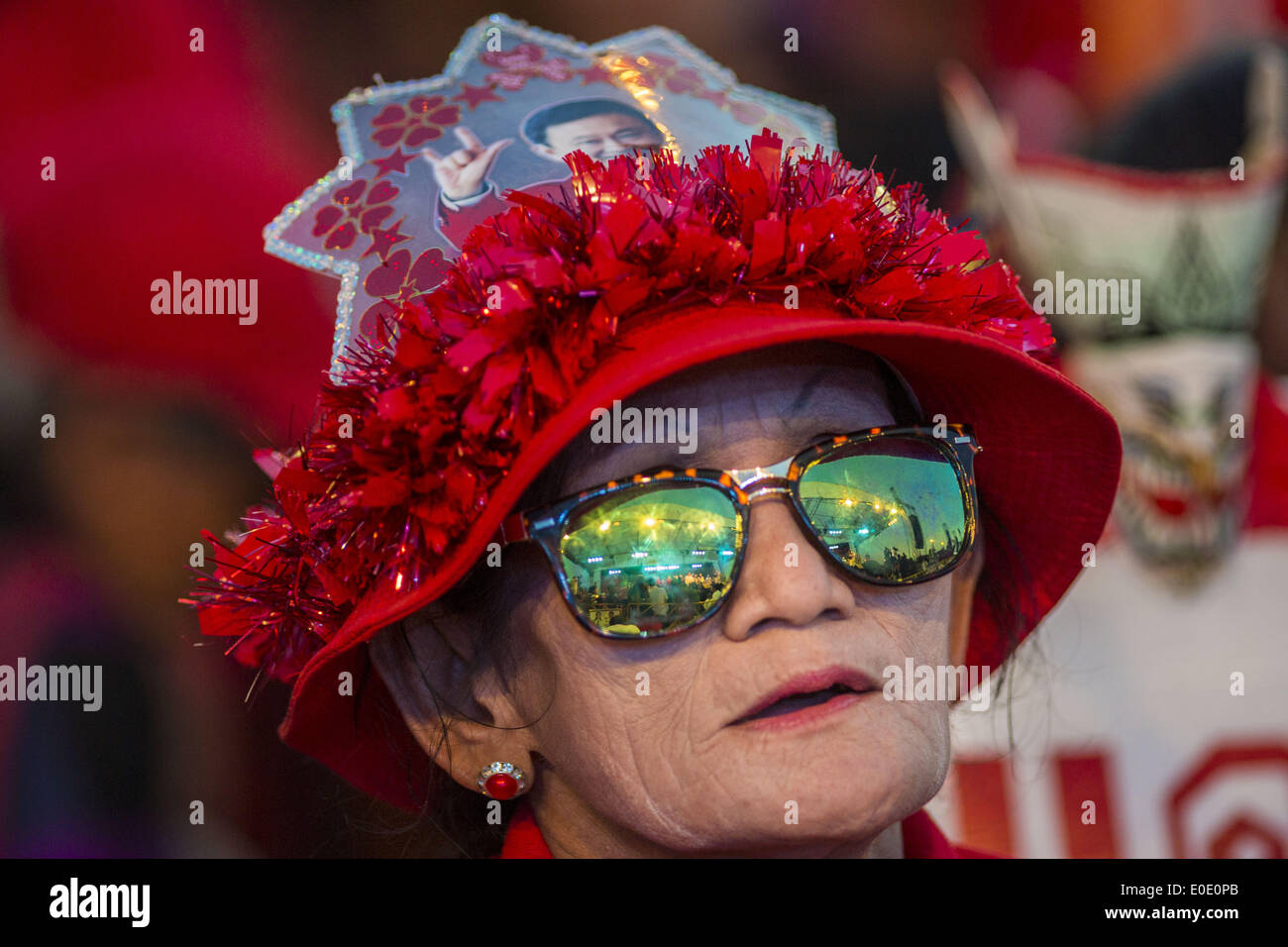 Bangkok, Thailand. 10th May, 2014. A Red Shirt supporter with a photo of ousted and exiled former Prime Minister Thaksin Shinawatra on her hat cheers for ousted Prime Minister Yingluck Shinawatra (Yingluck is Thaksin's sister) at a rally in Bangkok. Thousands of Thai Red Shirts, members of the United Front for Democracy Against Dictatorship (UDD), members of the ruling Pheu Thai party and supporters of the government of ousted Prime Minister Yingluck Shinawatra are rallying on Aksa Road in the Bangkok suburbs. Credit:  ZUMA Press, Inc./Alamy Live News Stock Photo