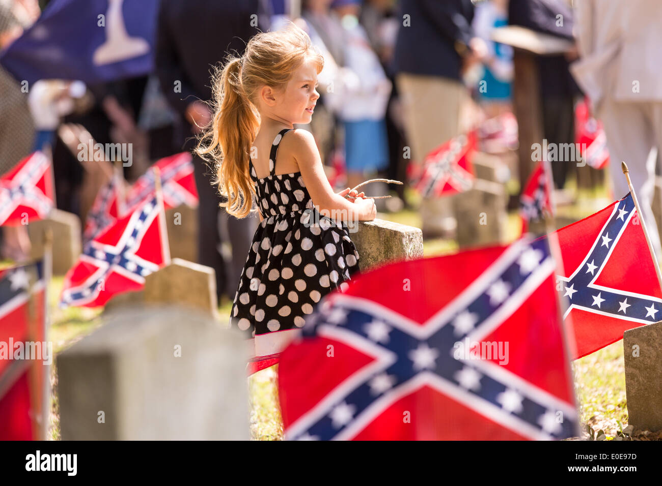 A young girl stands among Confederate flags decorating tombs of
