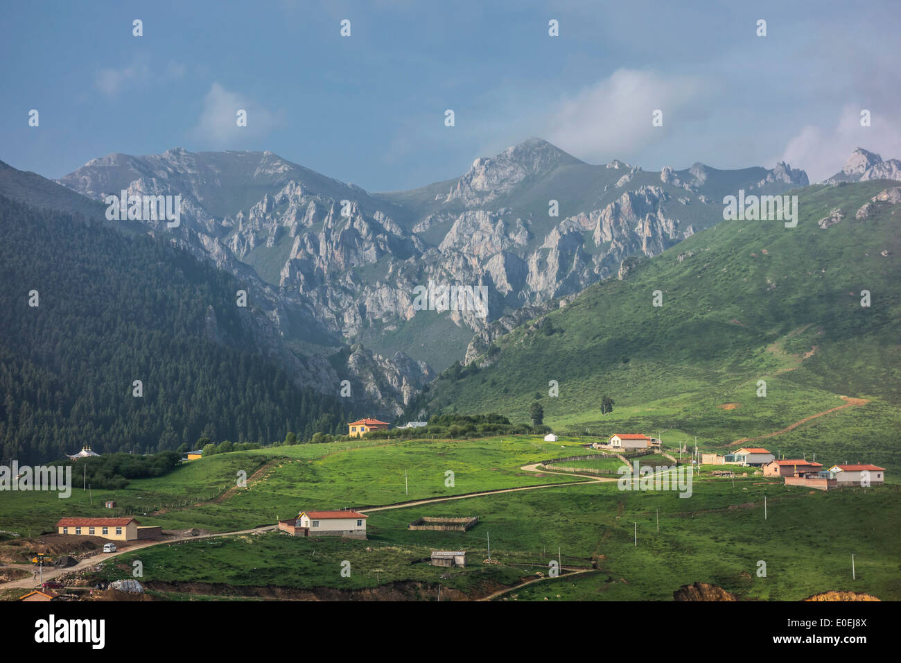 Idyllic mountain village nestled at the foot of majestic peaks under a blue sky in Sichuan, China Stock Photo