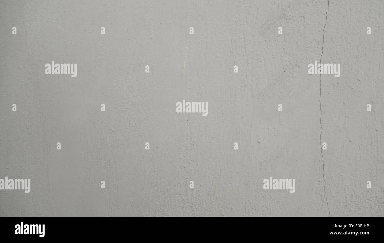 This textured concrete wall surface features a subtle, off-white color with a hairline crack that adds character. Stock Photo