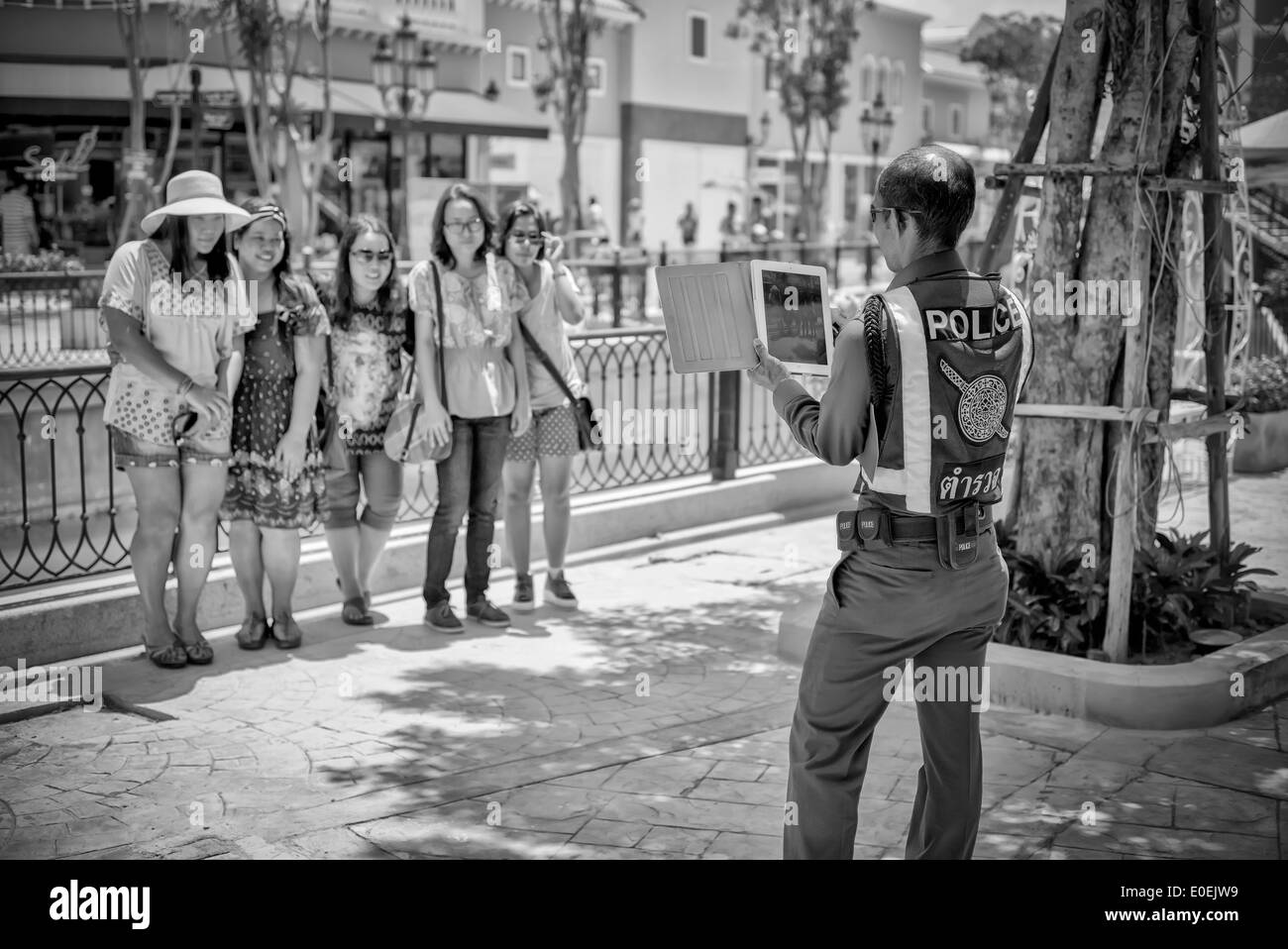 Thailand police officer assisting local tourist group by taking their photograph on an iPad tablet. Thailand S. E. Asia Black and white photography Stock Photo