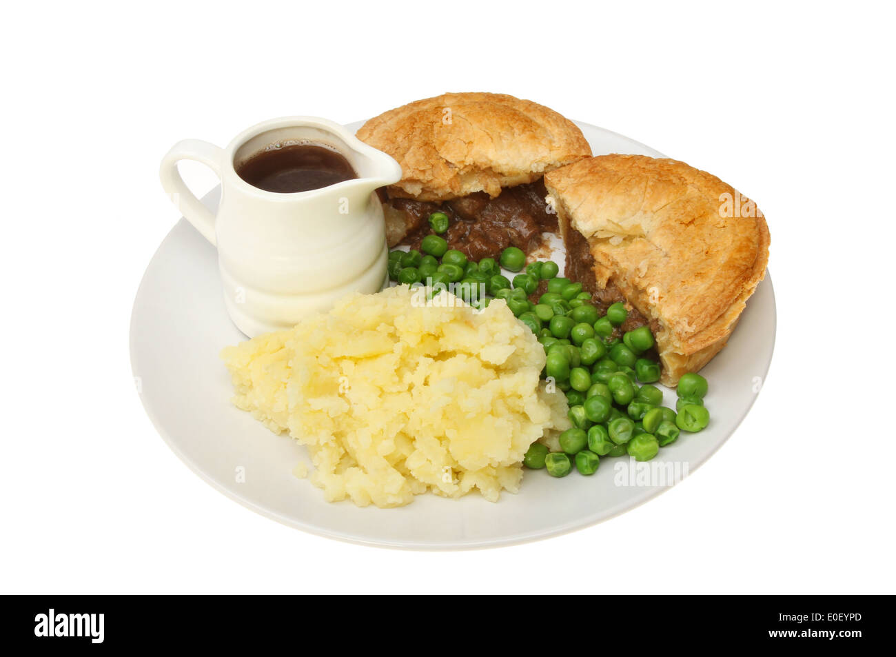 Meat pie, mashed potato and peas with a jug of gravy on a plate isolated against white Stock Photo