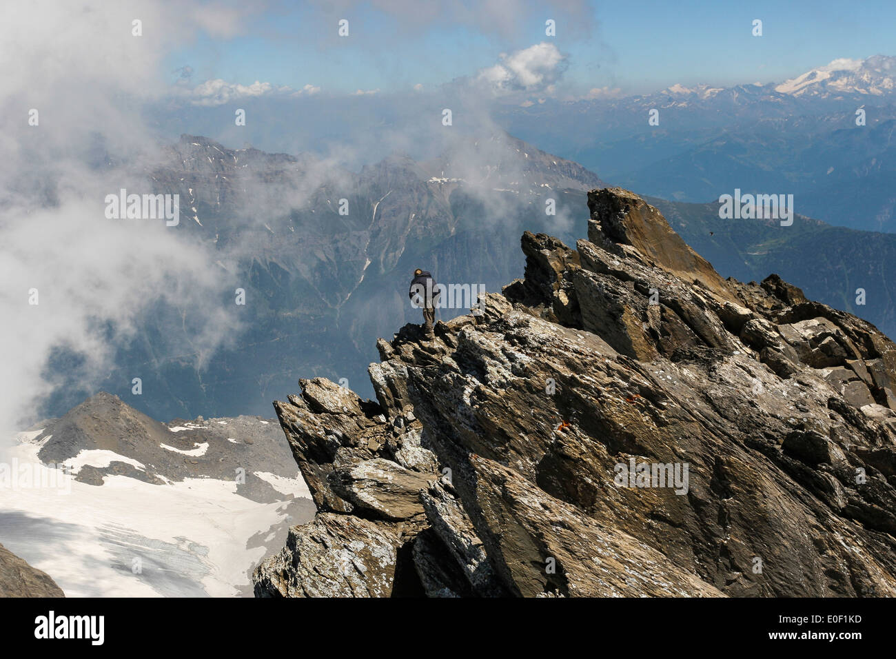 A man peers down from the sharp summit ridge of the Haute Cime peak of the Dents du Midi mountain range in Switzerland Stock Photo