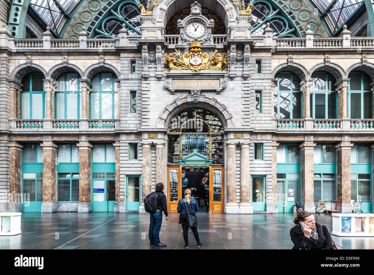 Young couple looks at the clock above the entrance hall of the Antwerpen-Centraal railway station. Stock Photo