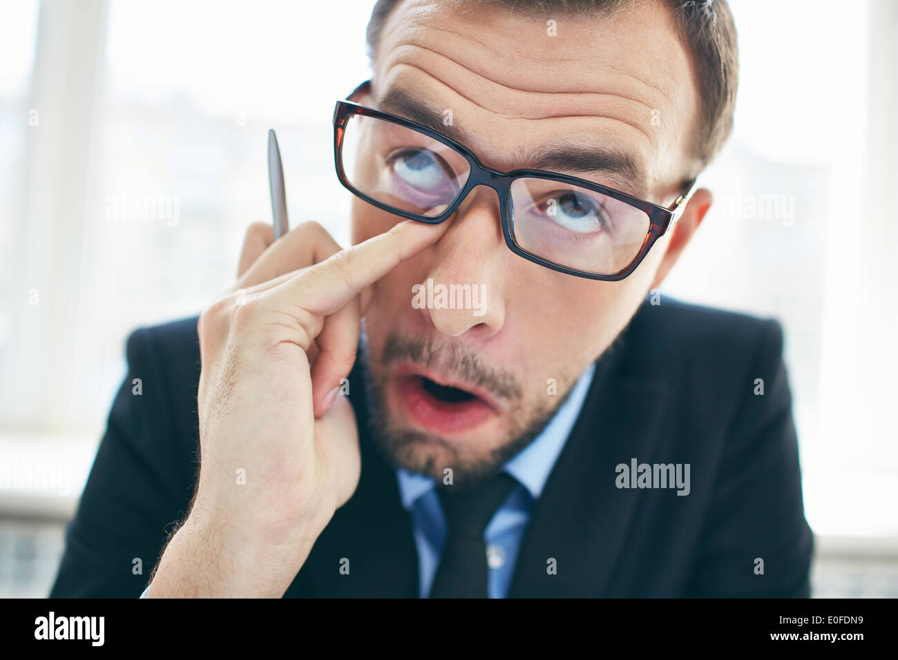 Face of funny businessman in eyeglasses rubbing eye Stock Photo