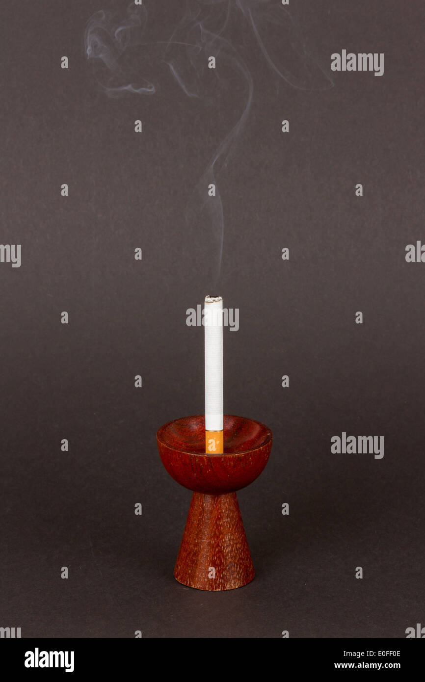 Burning cigarette in a candleholder on black background Stock Photo