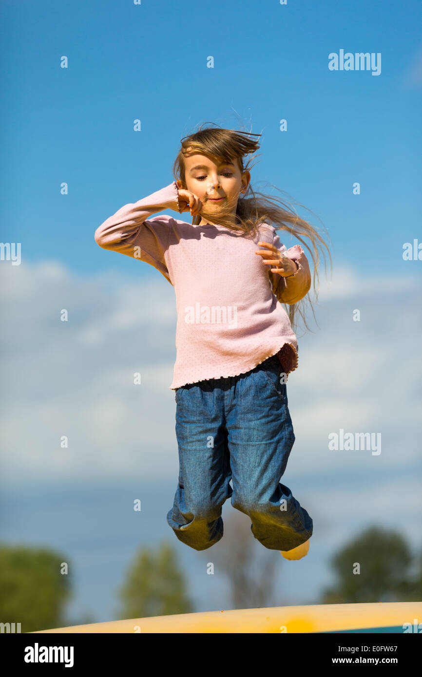 Girl jumping up and down on bouncy cushion outdoors during spring time