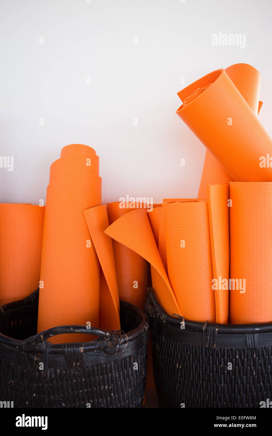 Seven orange yoga mats rolled up in baskets against white wall yoga