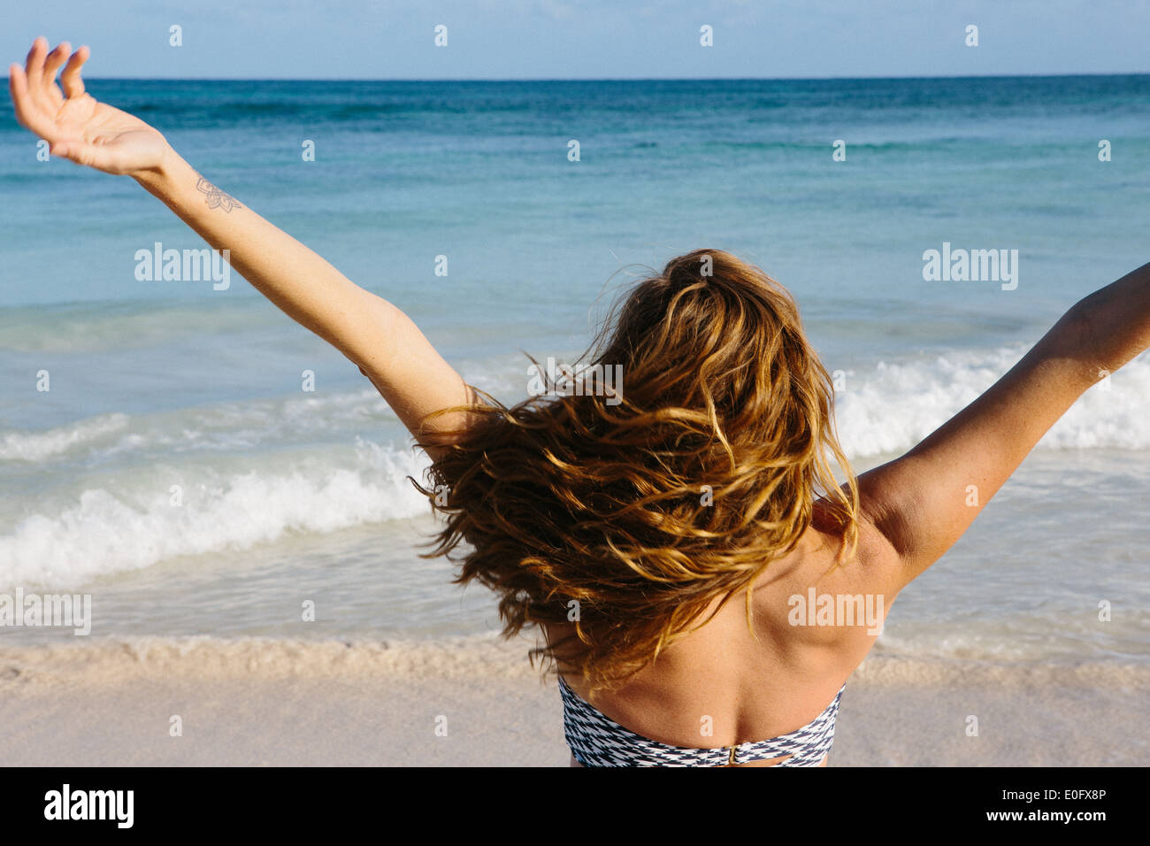 Woman with blond hair raising her arms up in front of the ocean Stock Photo