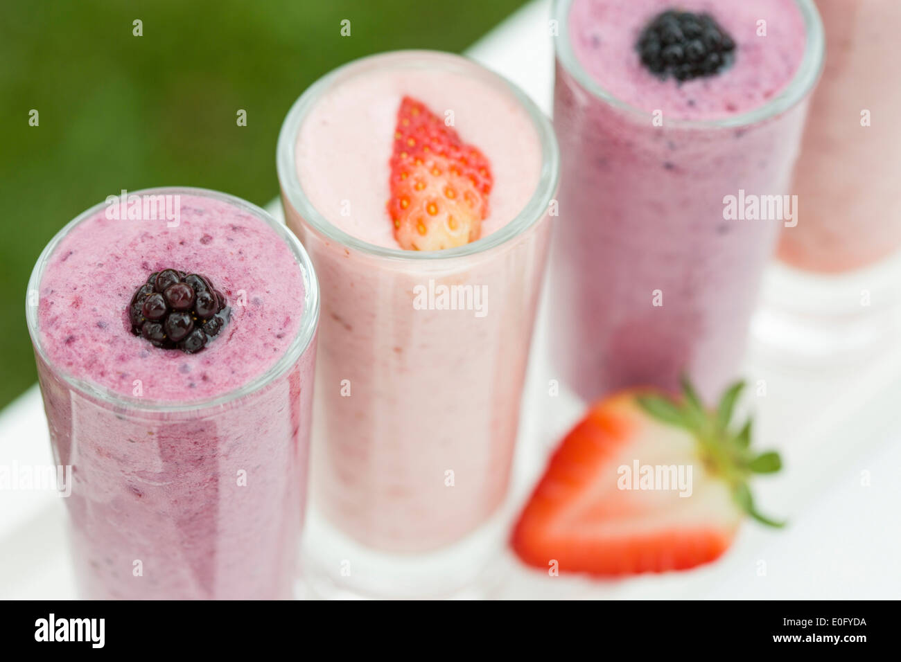 Strawberry and blackberry drinks in summer garden, served in tall shot glasses on white table Stock Photo